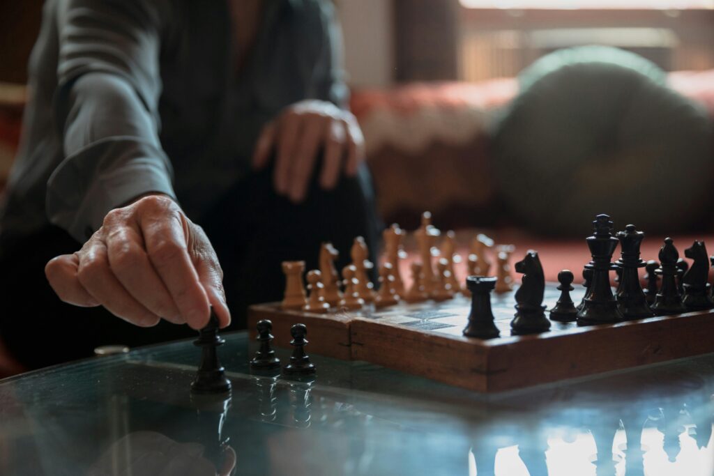 An adult in a cozy room makes a thoughtful move on a wooden chessboard.